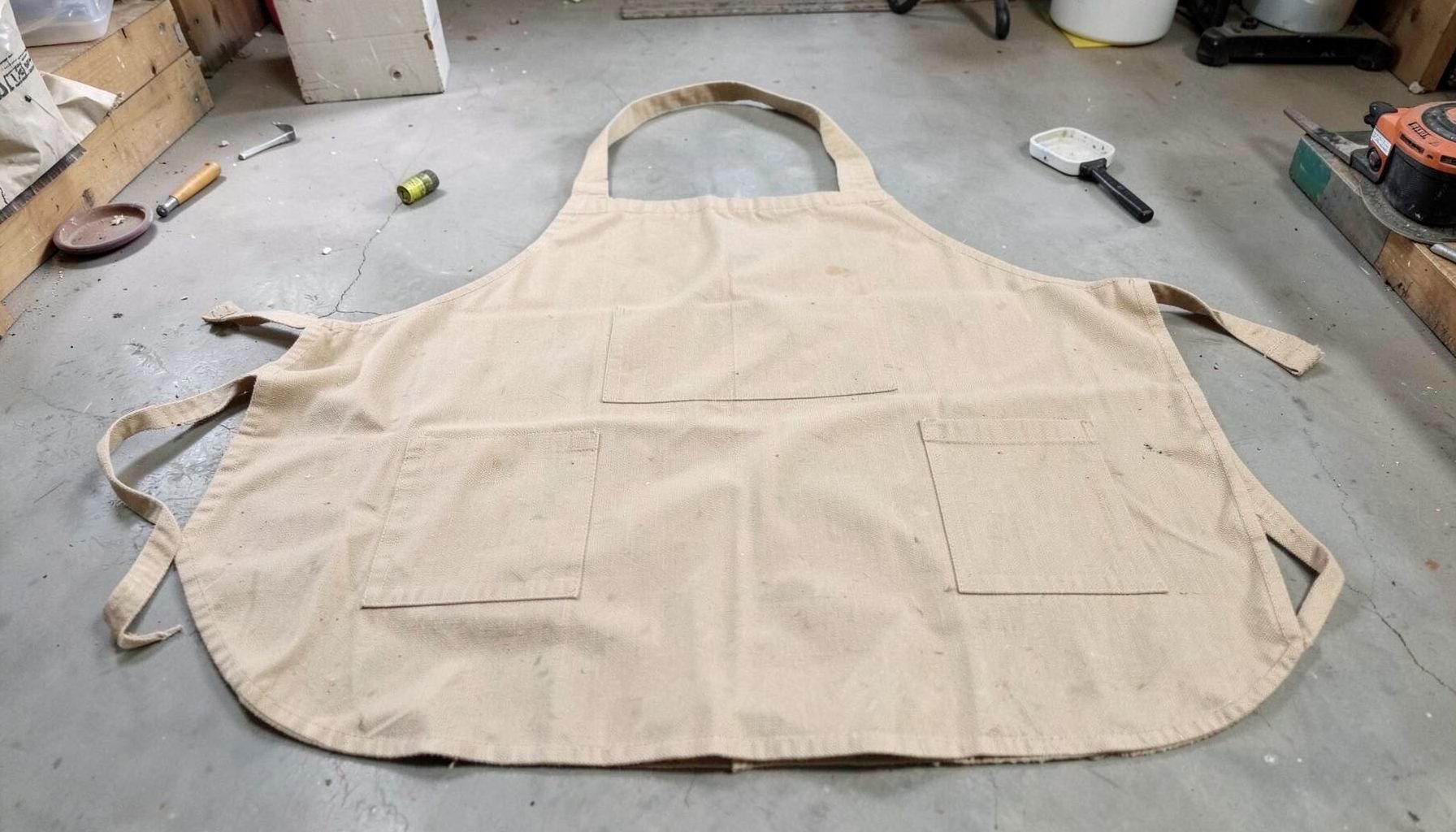 Canvas welding apron in natural tan fabric laid flat, simple workshop setting