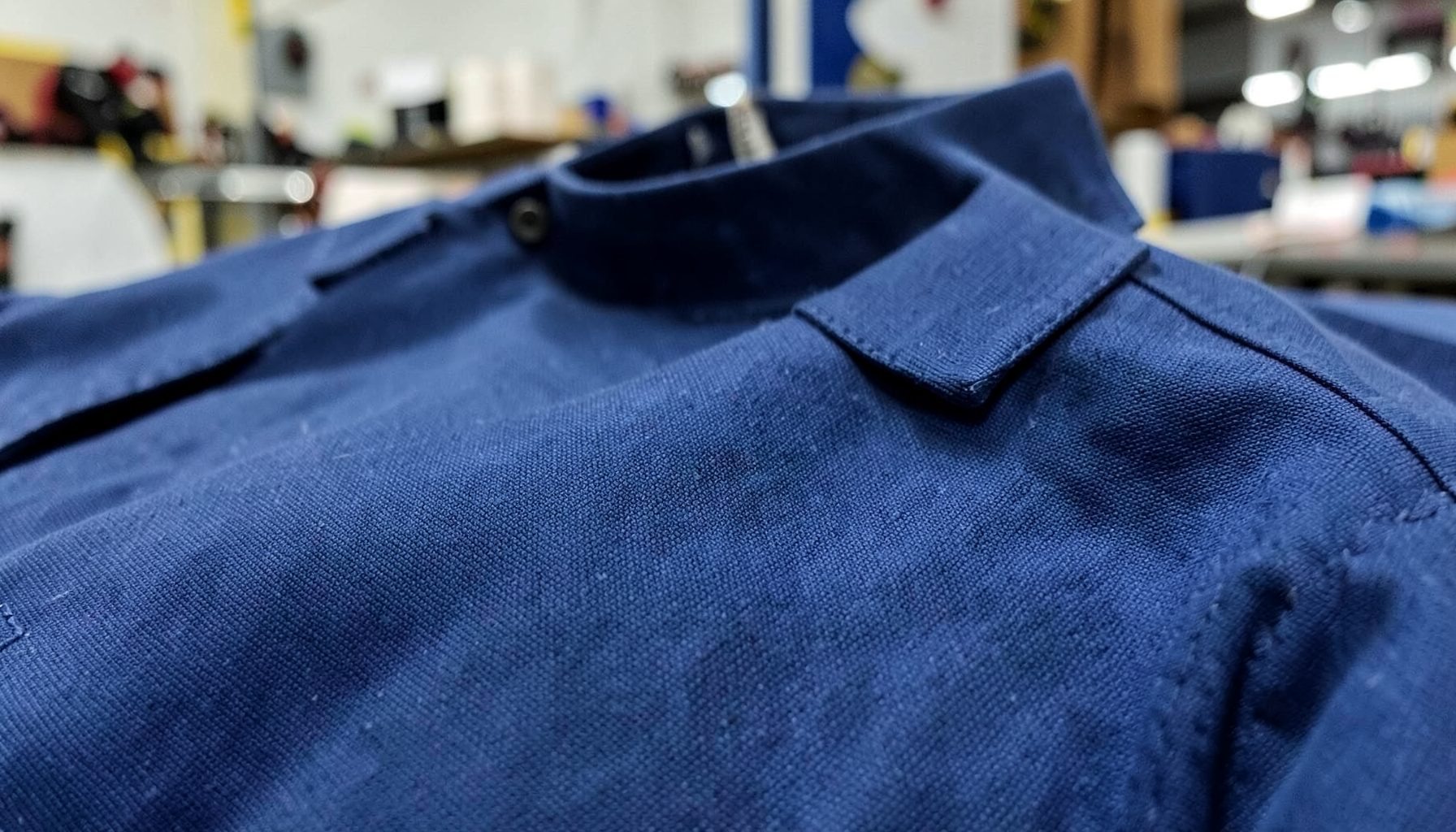 Close-up of a flame-resistant work shirt fabric in navy blue, textured weave visible, workshop setting