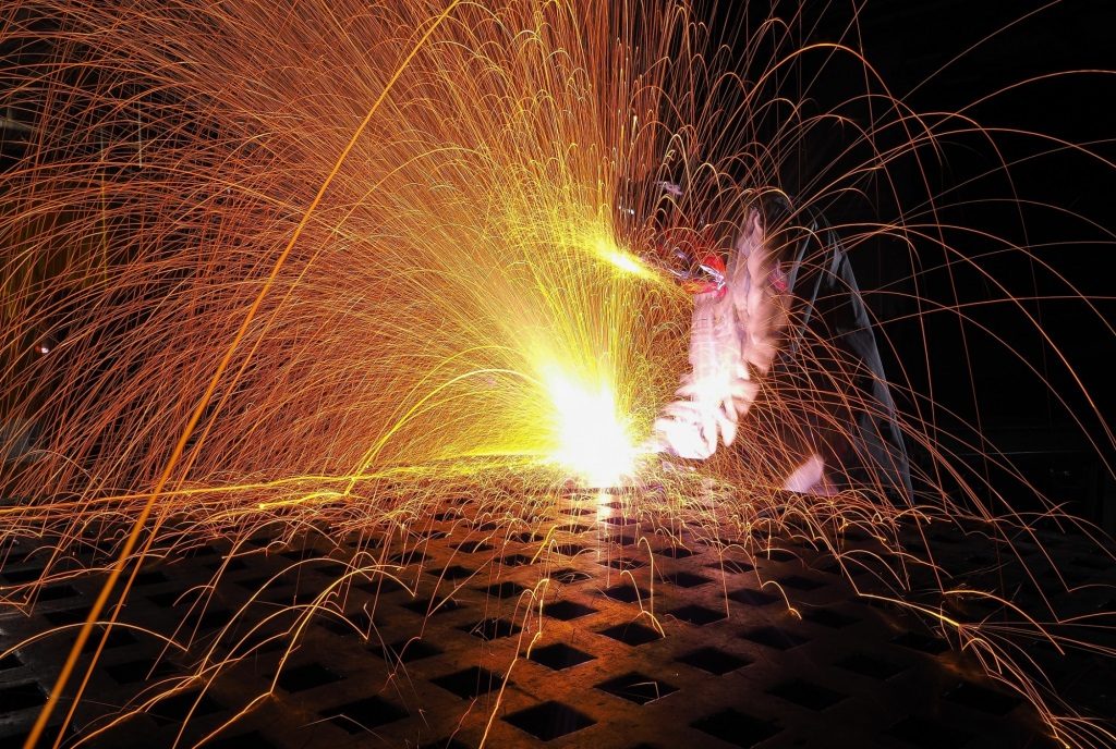 Bright orange and yellow sparks flying from metalwork in a dark setting, dramatic mood